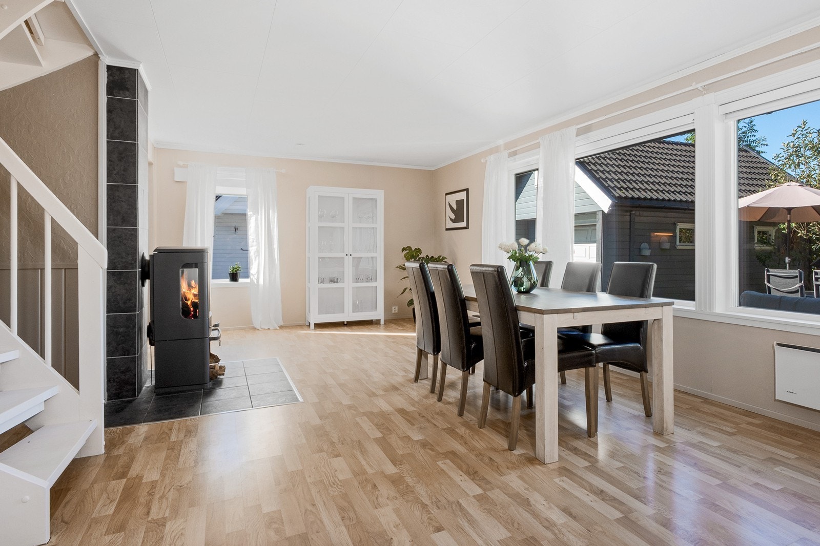 Spisestuen fungerer som et naturlig bindeledd mellom kjøkken og sofadel, mens en koselig peisovn sentralt i rommet bidrar til varme. Galleribilde