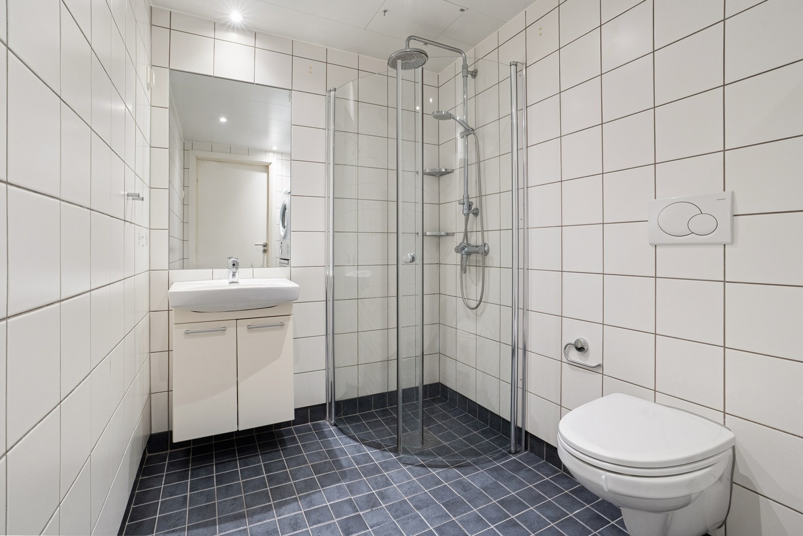 Flislagt og delikat baderom med downlights og gulvvarme som gir ekstra komfort. Rommet er innredet med servant med slette fronter, veggmontert toalett og dusjhjørne med to svingbare glassdører. Galleribilde