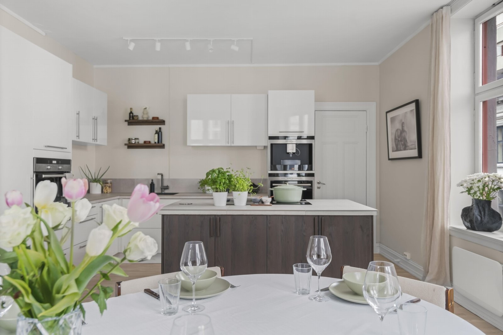 Innredningen består av slette hvite fronter kombinert med mørkere finér på kjøkkenøyen, en gjennomført og moderne stil Galleribilde