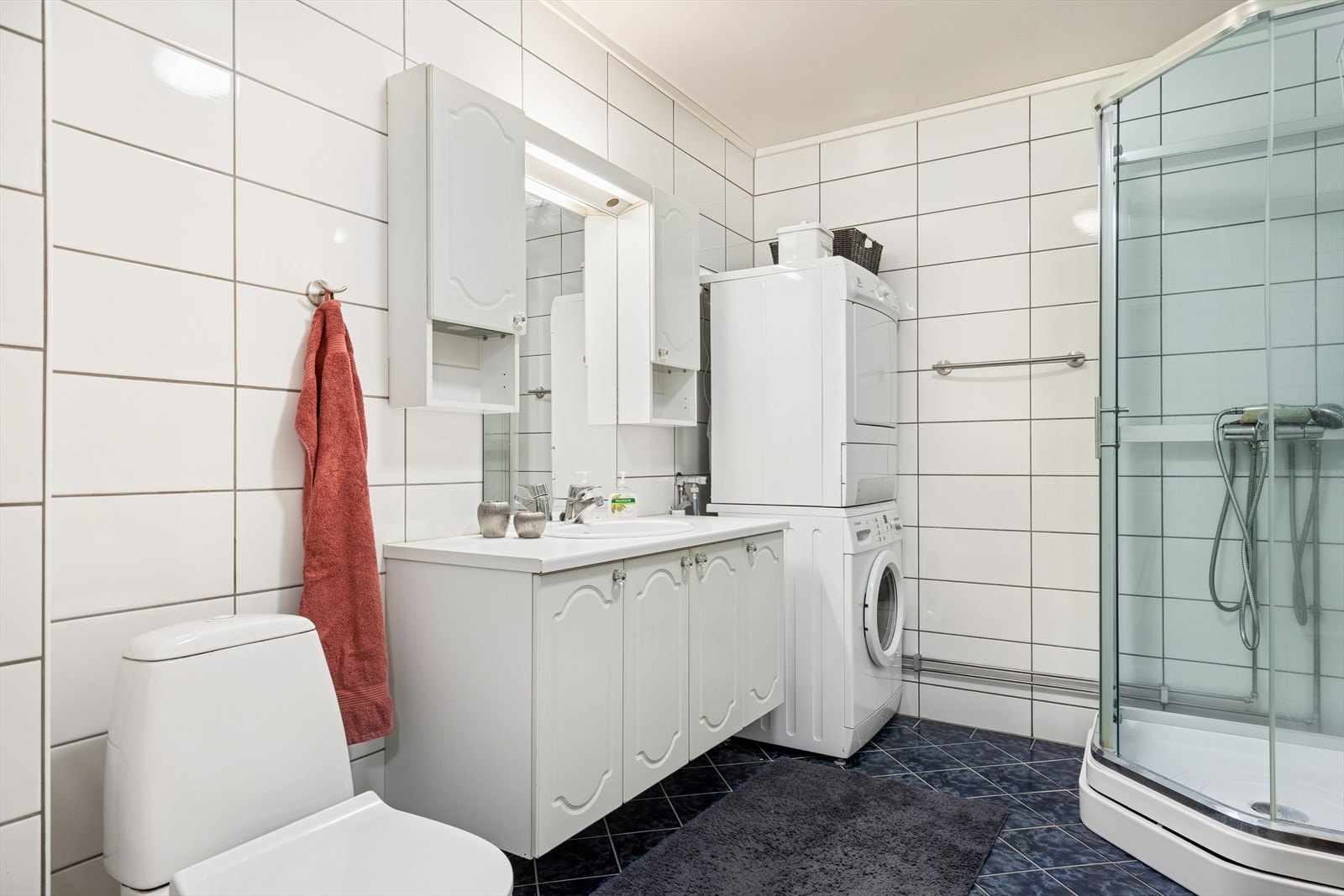 Badet er utstyrt med dusjkabinett, gulvstående toalett og opplegg for både vaskemaskin og tørketrommel. Galleribilde