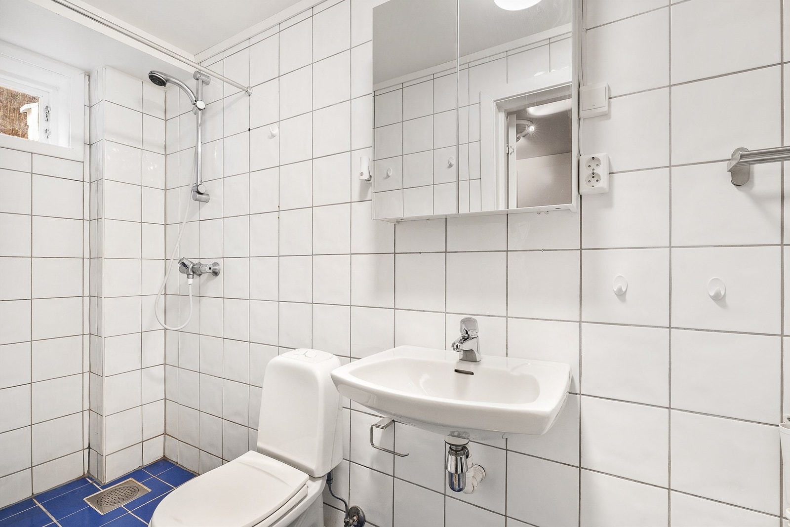 Badet har gulvmontert toalett, dusjhjørne med dusjforheng, servant og opplegg for vaskemaskin Galleribilde