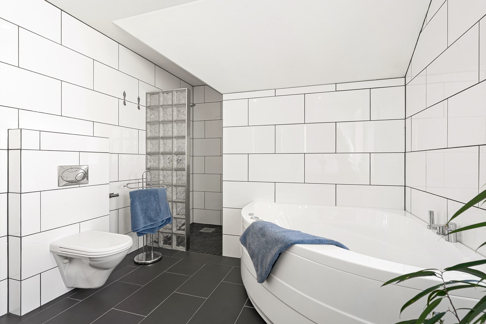 Badet ligger vegg i vegg med vaskerommet og er klassisk helfliset med varme i gulvet. Det inneholder et hjørnebadekar, dusjnisje, vegghengt toalett, samt baderomsinnredning med dobbel vask og speil over. Galleribilde