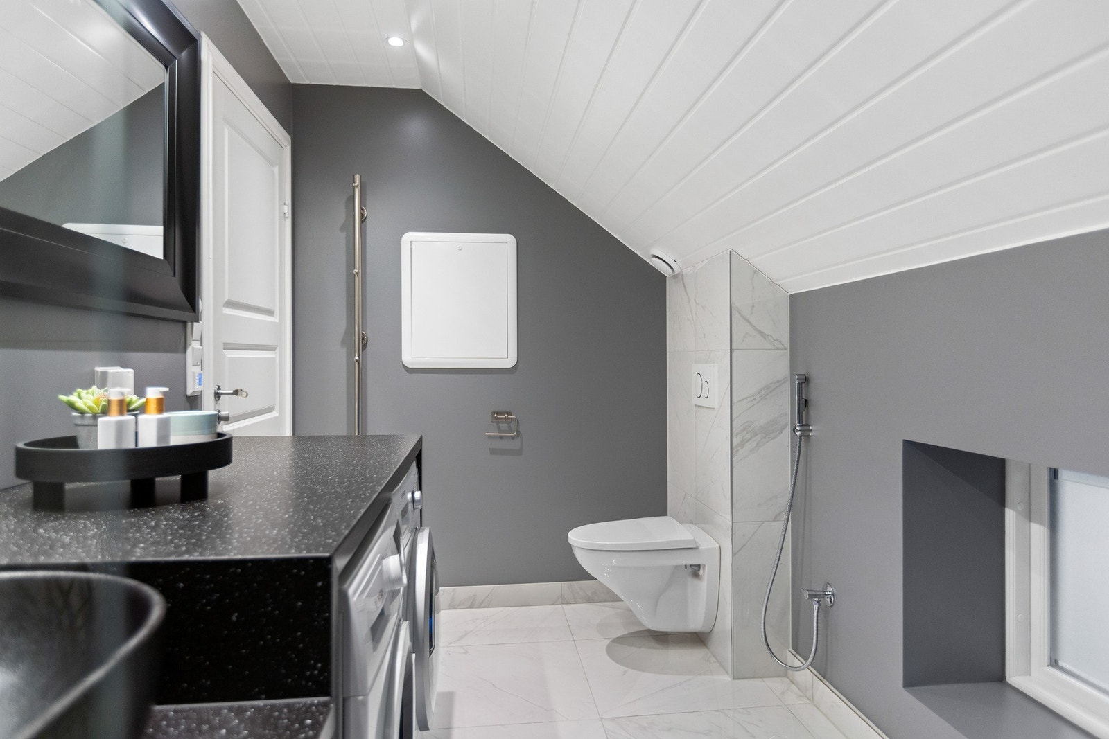 Her får du vegghengt toalett, dusjhjørne ved siden av toalettet og en moderne baderomsinnredning med mørk benkeplate. Galleribilde