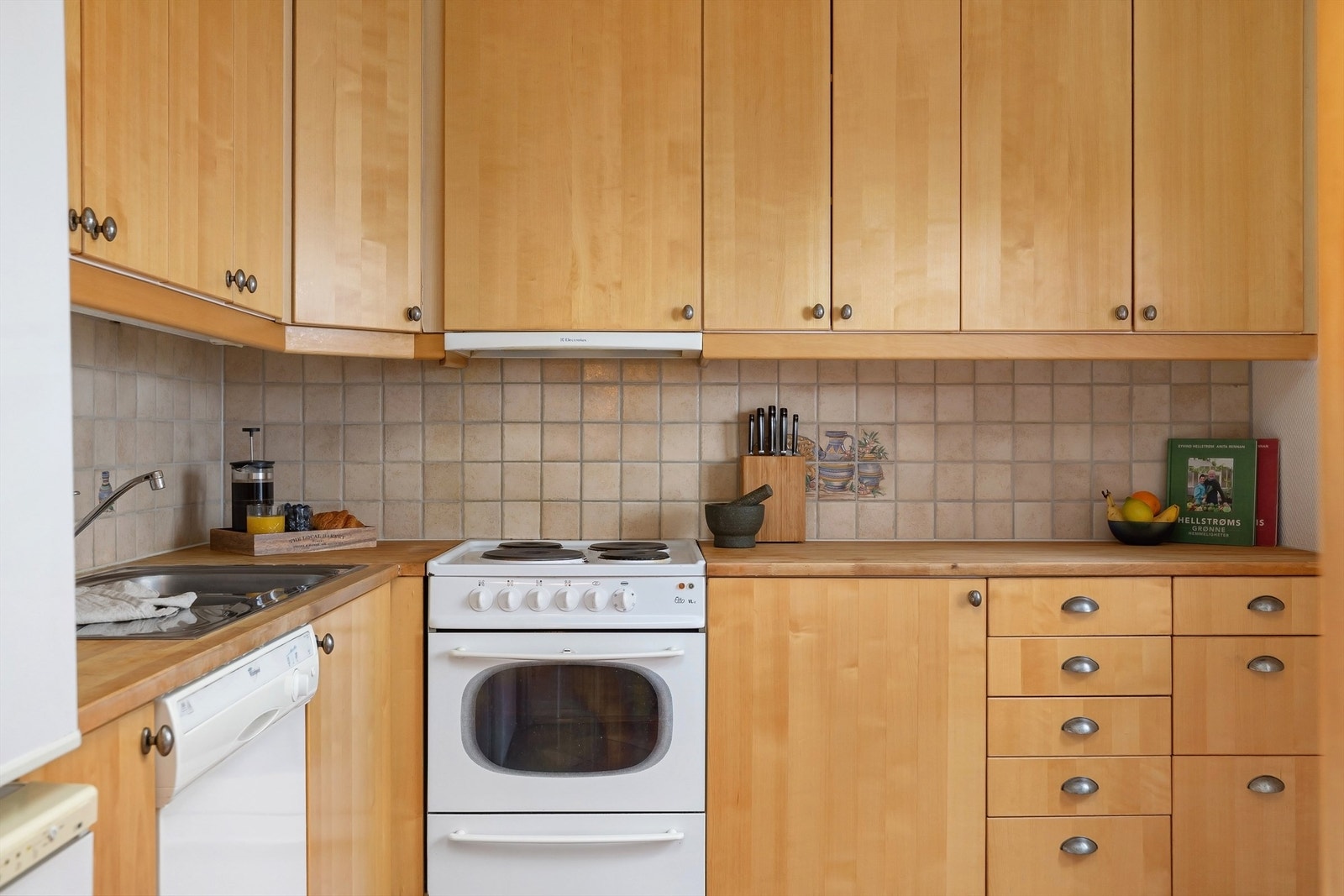 Kjøkkeninnredning med slette fronter, fliser mellom overskap og benkeplate av tre samt nedfelt oppvaskkum med ett-greps blandebatteri. Galleribilde