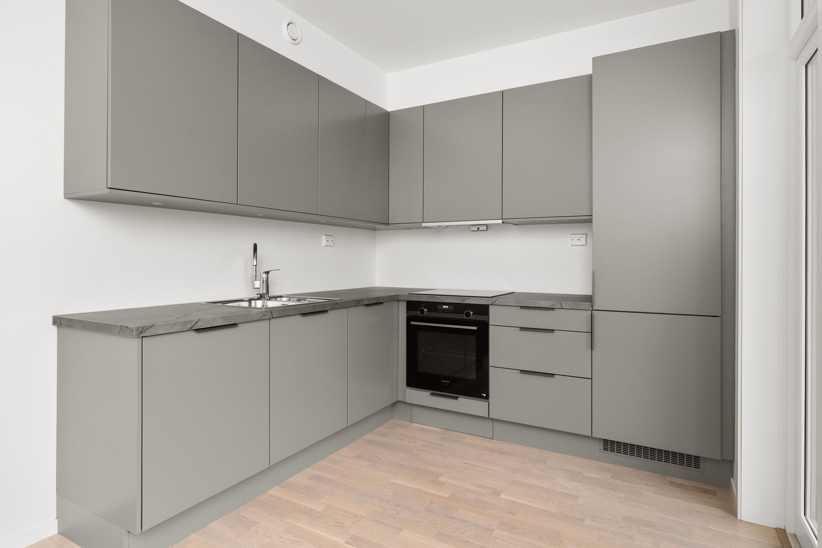 Moderne kjøkken med grå skapfronter, integrerte hvitevarer og lys parkett. Praktisk utforming med god lagringsplass. Galleribilde