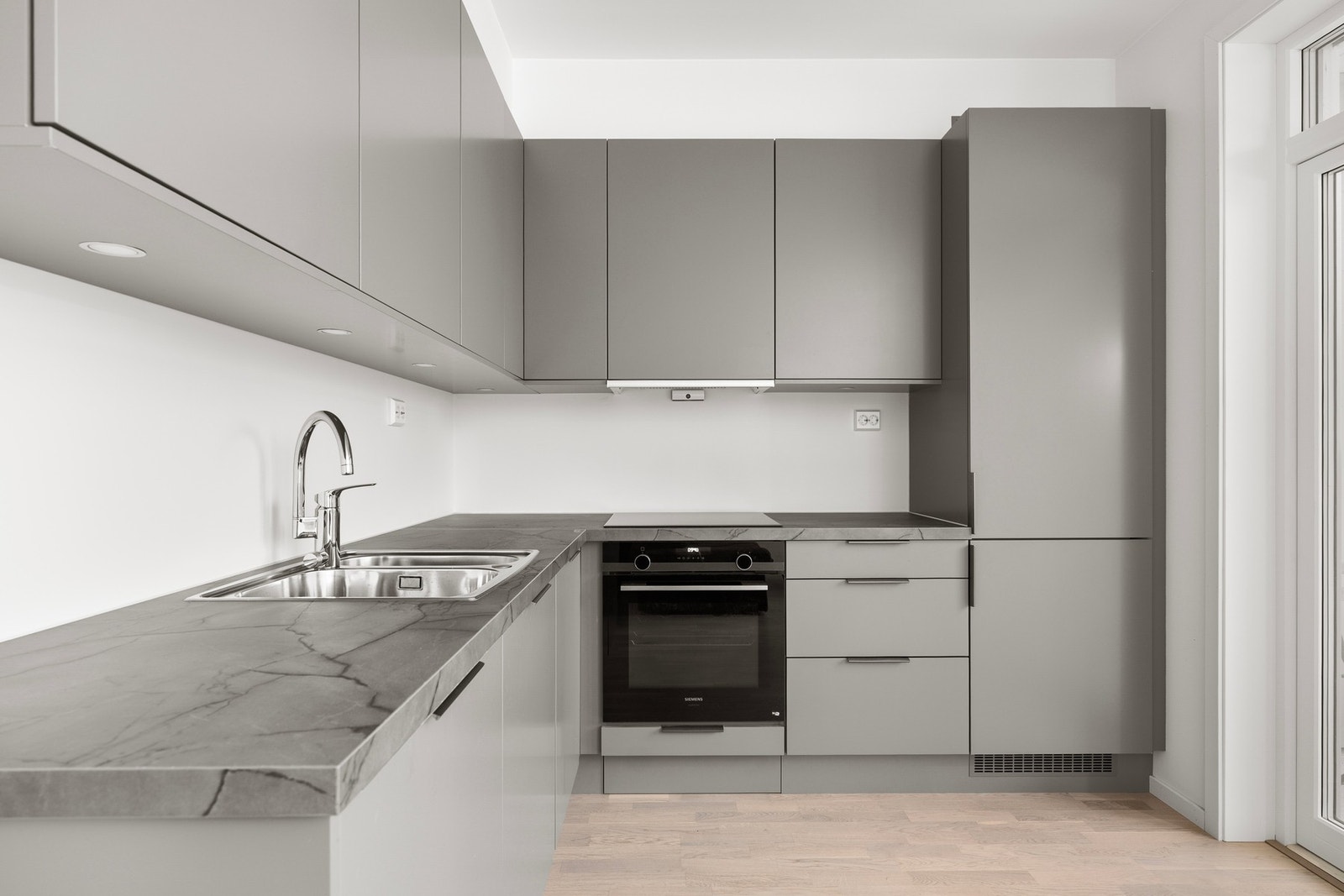 Moderne kjøkken med grå skapfronter, integrerte hvitevarer og lys parkett. Praktisk utforming med god lagringsplass. Galleribilde