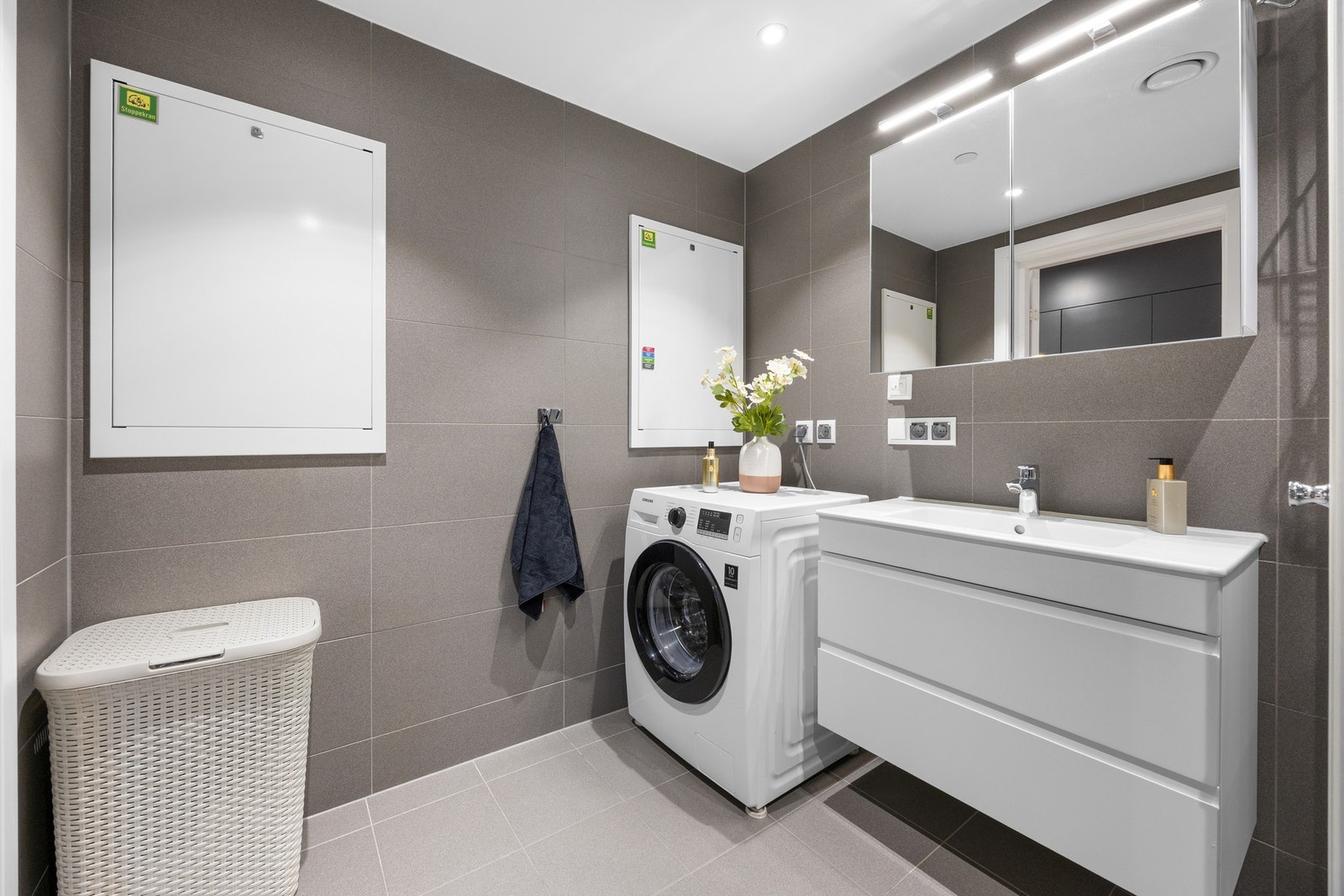 Delikat bad med flislagte overflater og vannbåren gulvvarme. Baderomsinnredningen består av moderne servantmøblement med heldekkende hvit blank vask og speil med integrert LED lys. Galleribilde