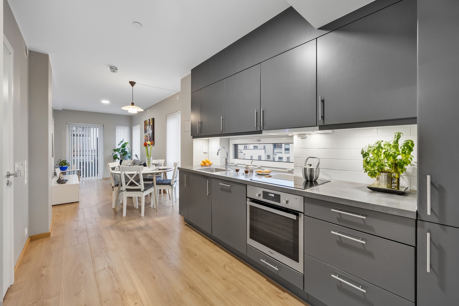 Stilrent kjøkken fra 2021 i åpen løsning mot stuen. De store vindusflatene sørger for rikelig med lys og bidrar til gode arbeidsforhold ved matlagingen. Galleribilde