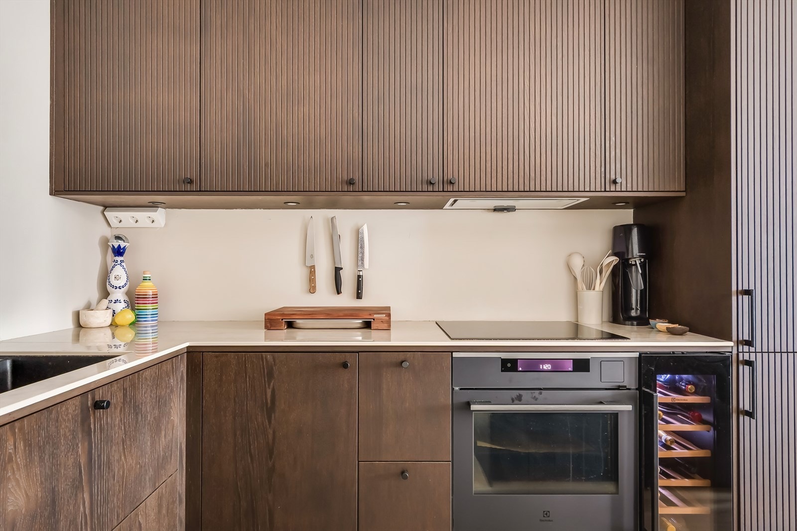 Lekkert og moderne kjøkken fra 2025 utstyrt med integrerte hvitevarer som platetopp, stekeovn, vinskap, oppvaskmaskin og kjøl/fryseskap. Galleribilde