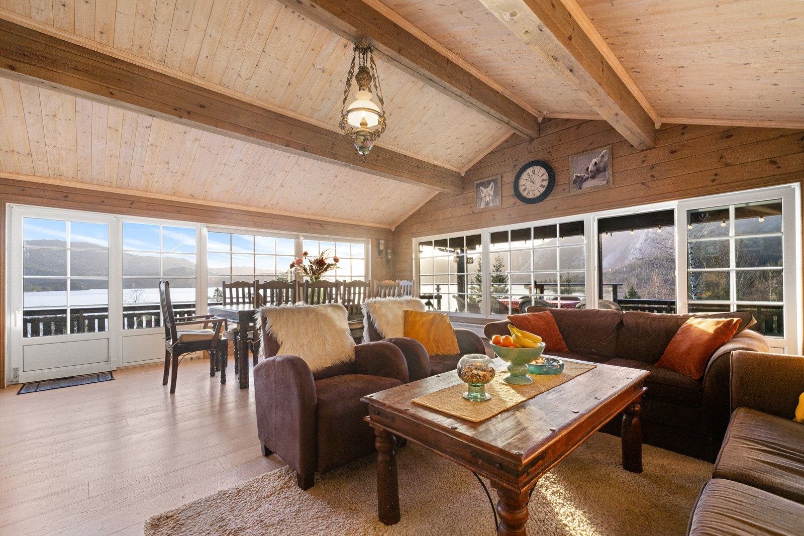 Romslig og lys stue i åpen løsning med spisestue, preget av god takhøyde, synlige bjelker og gjennomgående trepanel som gir en lun og klassisk hyttefølelse. Galleribilde