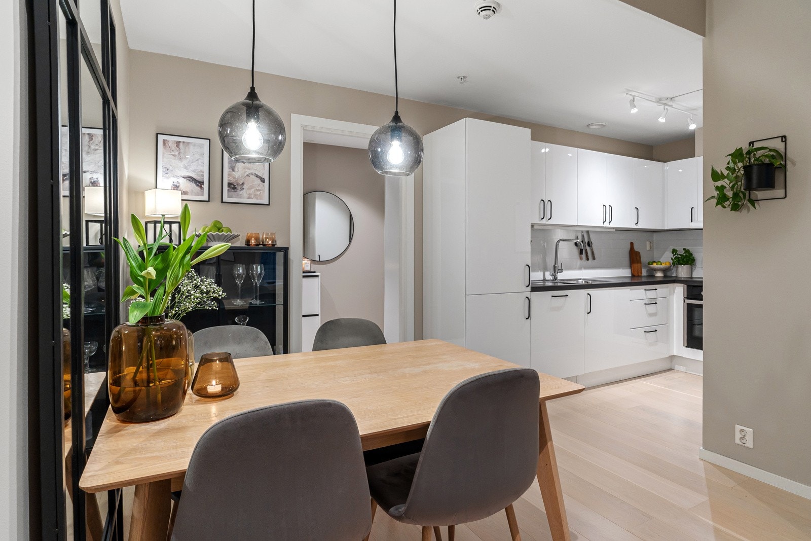 Pent kjøkken fra Aubo med hvite, slette høyglansfronter, stålhåndtak og overskap med benkebelysning. Galleribilde