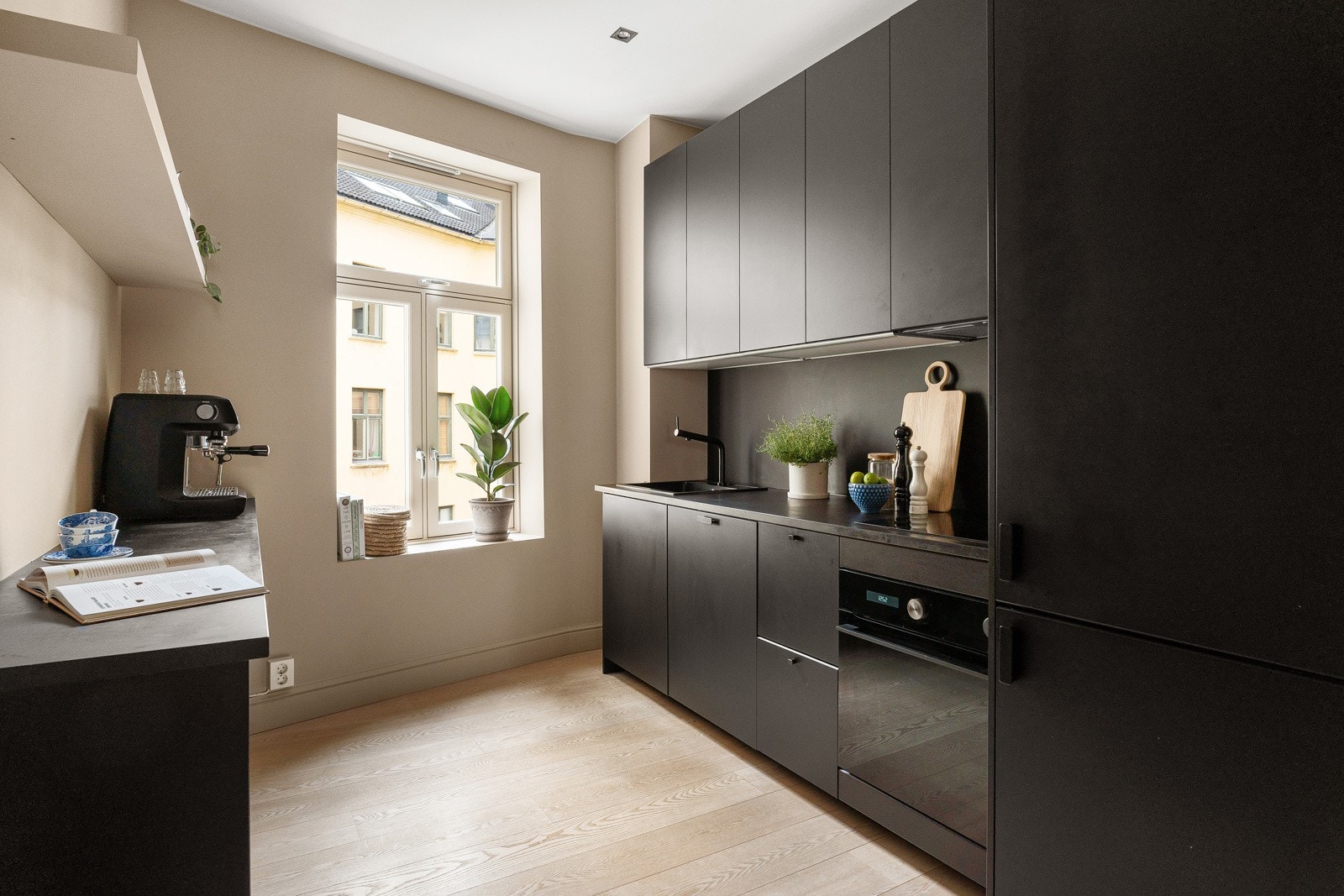 Stilrent og moderne kjøkken med sorte, matte fronter og mørke veggplater over benk. Galleribilde