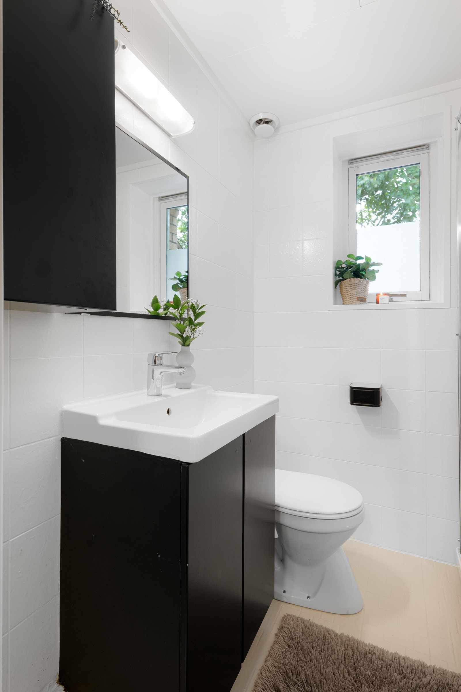 Sort baderomsinnredning med ovenpåliggende servant, speil med hylle og belysning over, samt ekstra vegghengt skap. Galleribilde