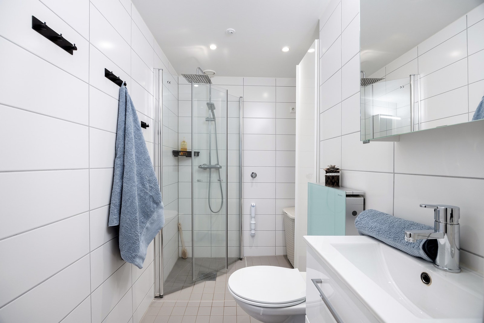 Badet er pent flislagt på gulv og vegger med vannbåren varme. Badet er innredet med vegghengt servantskap, ovenpåliggende servant og speilskap med belysning og dusjsone med innfellbare dører i glass. Galleribilde