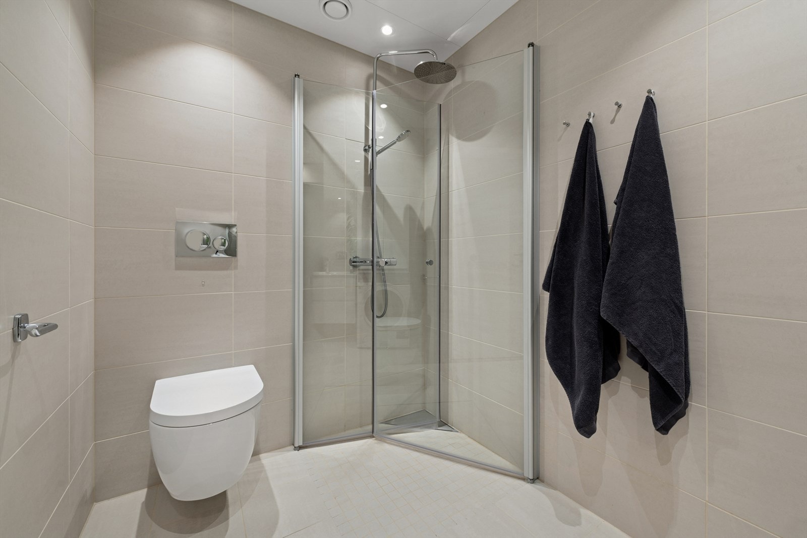 Helfliset baderom utstyrt med vegghengt toalett, dusj, servant med underskuffer og opplegg for vaskemaskin. Galleribilde