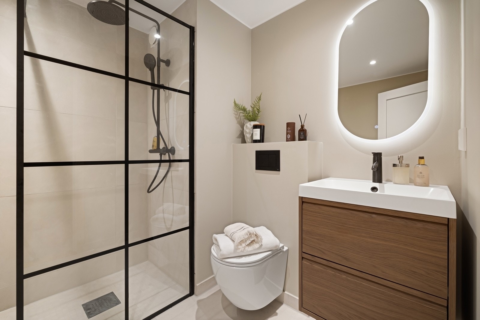 Baderom 2 (Rehabilitert 2025) - Bad med flislagt gulv og varmekabler. Vegger med fliser og malte flater.Speil med belysning, downlights, servant med innredning, dusjhjørne med glassvegg og vegghengt toalett Galleribilde