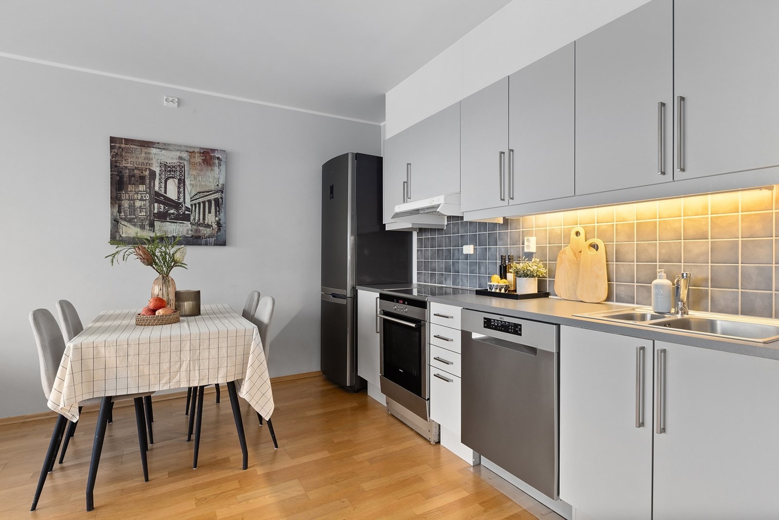 Kjøkken med glatte fronter, fliser over benk og benkeplate i laminat med dobbel stålkum. Galleribilde