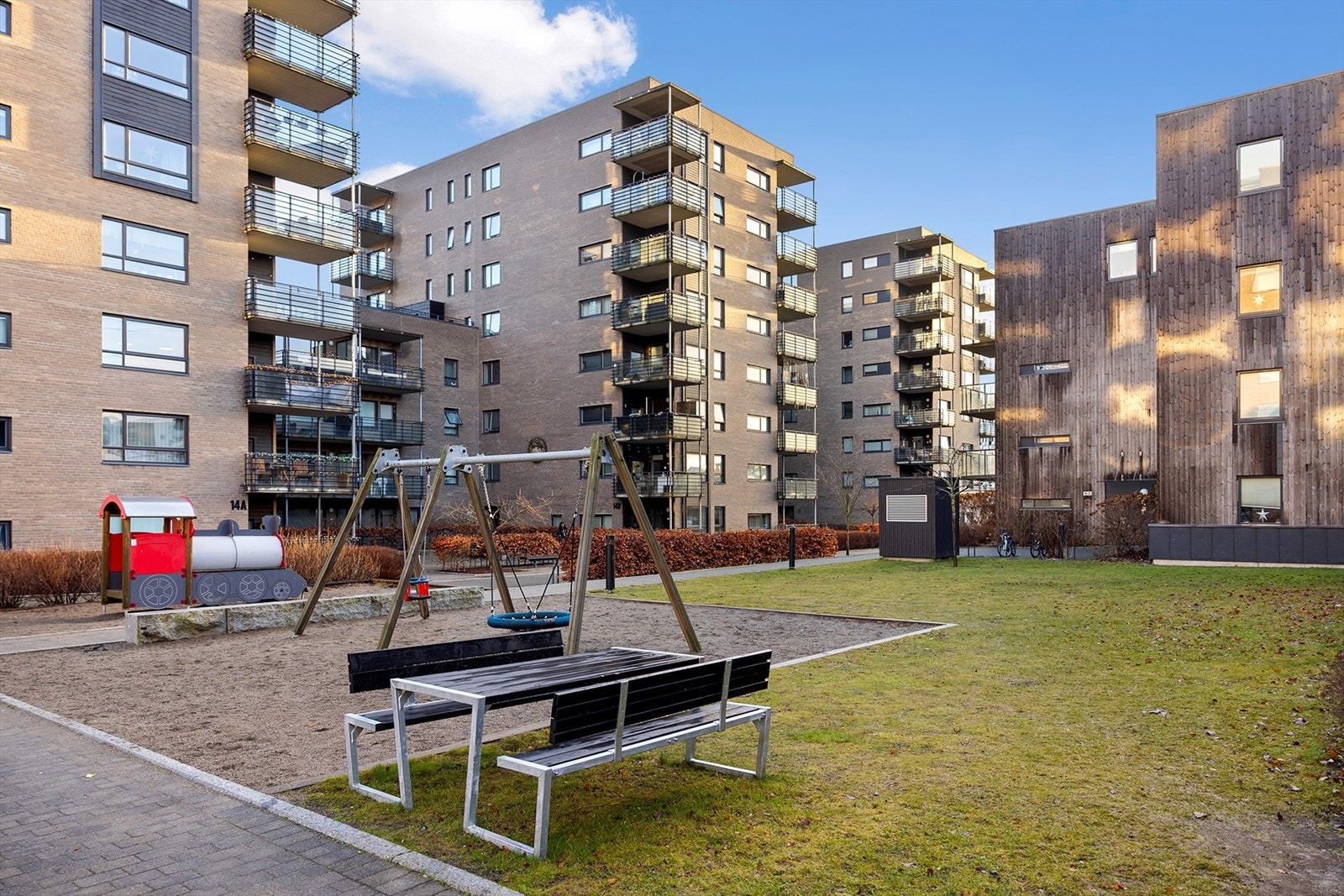Pent opparbeidet gårdsrom med gressplen, busker, beplantning, sittegrupper og lekeområder. Galleribilde