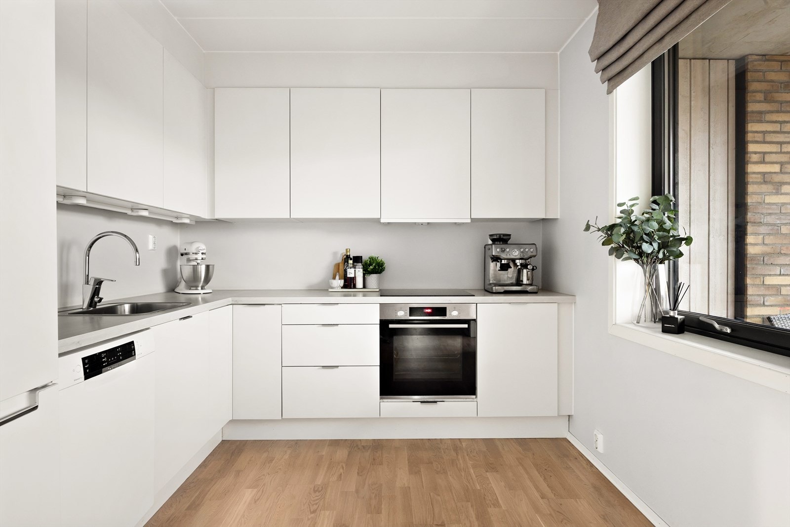 Stilrent kjøkken med lyse, glatte fronter. Induksjonstopp og stekeovn er integrert i innredningen. Galleribilde