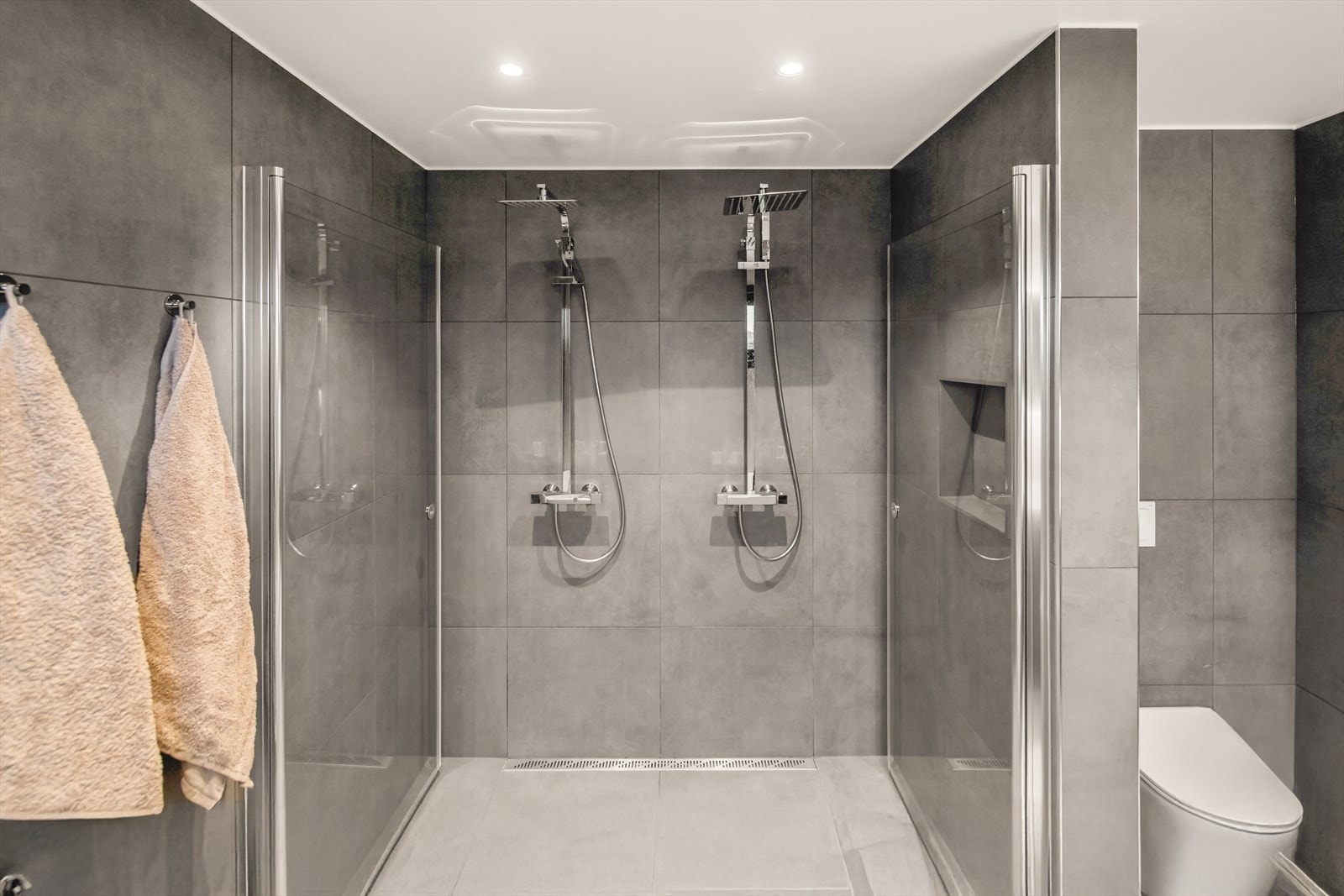 Vegger og gulv er kledd med store fliser i ulike grånyanser, og badet har downlights, varmekabler og vegghengt toalett. Galleribilde