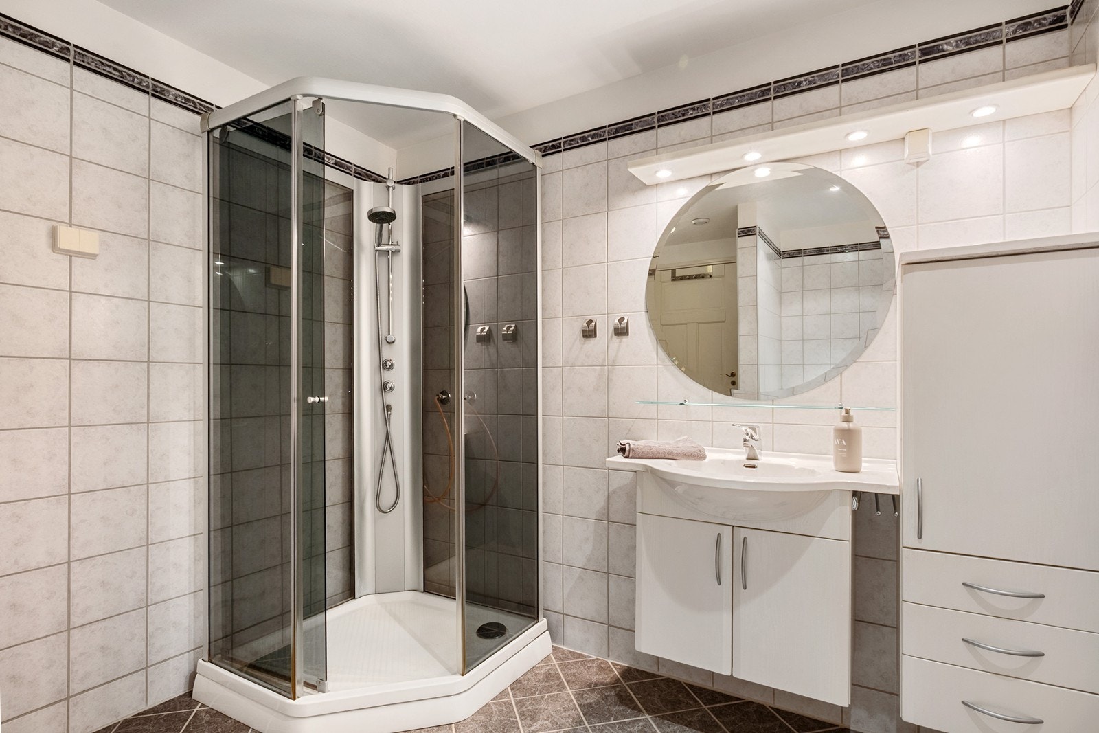 Badet har flislagte overflater i gråtoner og gulvvarme. Innredningen består av dusjkabinett, toalett, servantskap og høyskap. Galleribilde