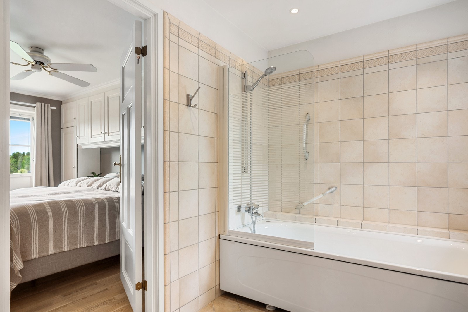 Badet har flislagte overflater, gulvvarme og downlights, badekar med dusjløsning, toalett og skap- og skuffeinnredning. Galleribilde