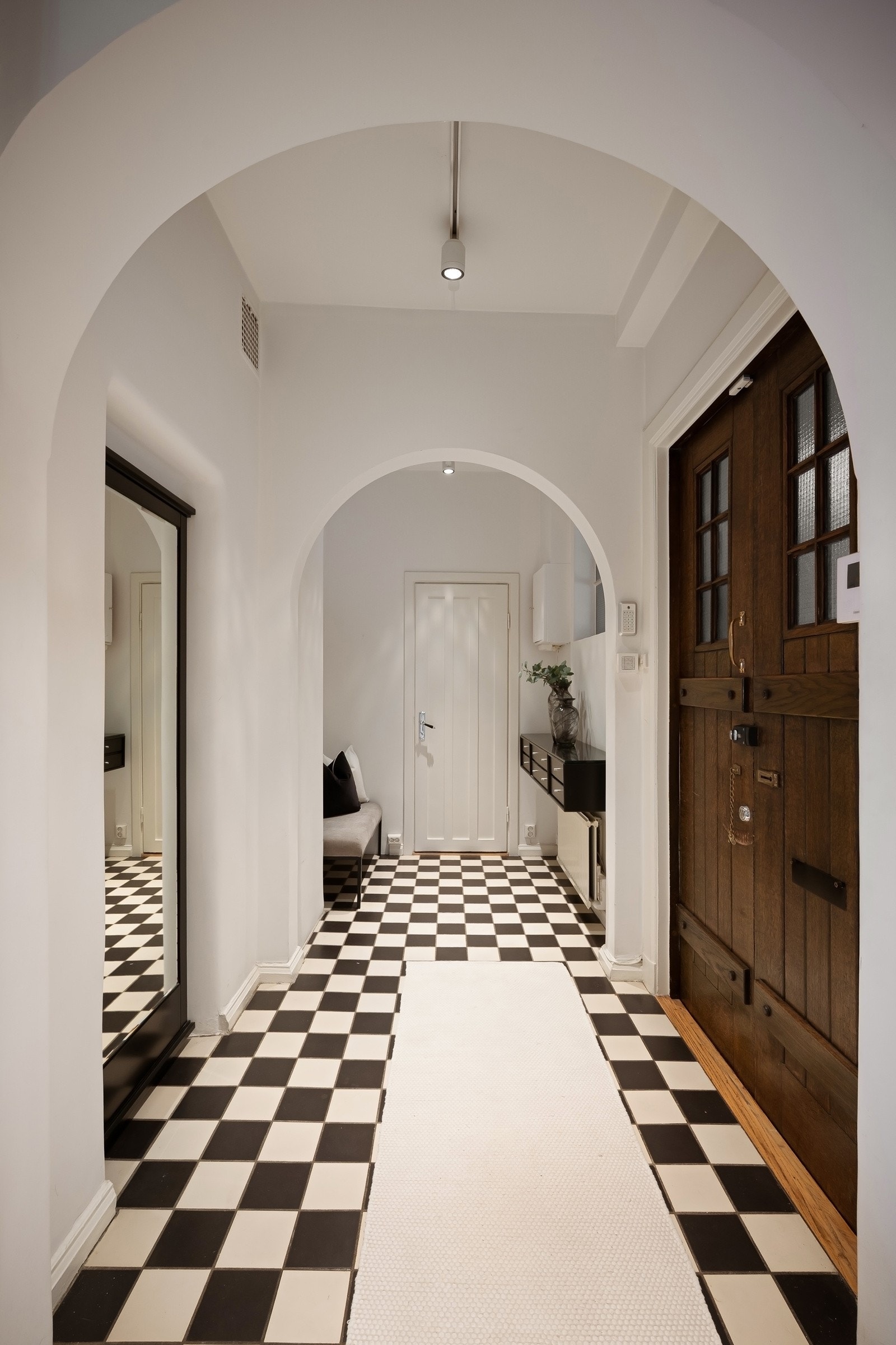Inngangspartiet er innbydende med flislagt gulv i sjakkbrettmønster, buevindu med sorte sprosser mot oppgangen og karakteristiske bueåpninger som romdeler. Galleribilde