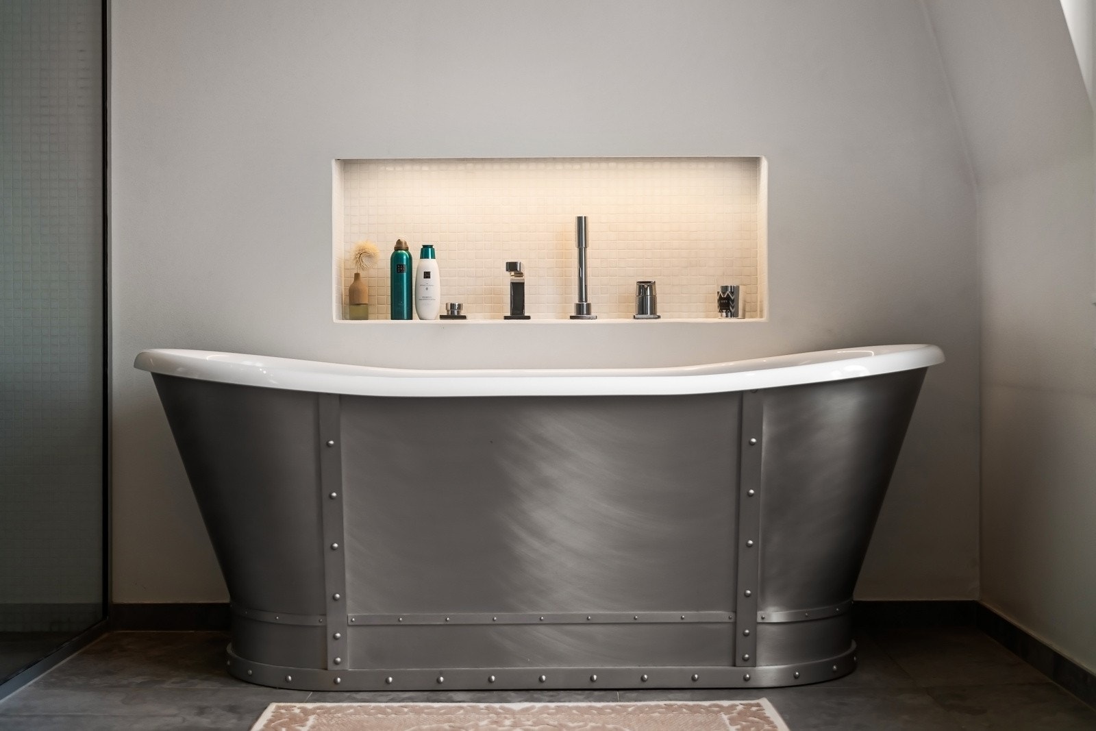 Badekaret er frittstående, holdt i et rustikk design, med belyst nisje for velværeprodukter, og dusjnisjen har takmontert regnfallsdusj, en hånddusj, glassvegg og sjamponisje med belysning. Galleribilde