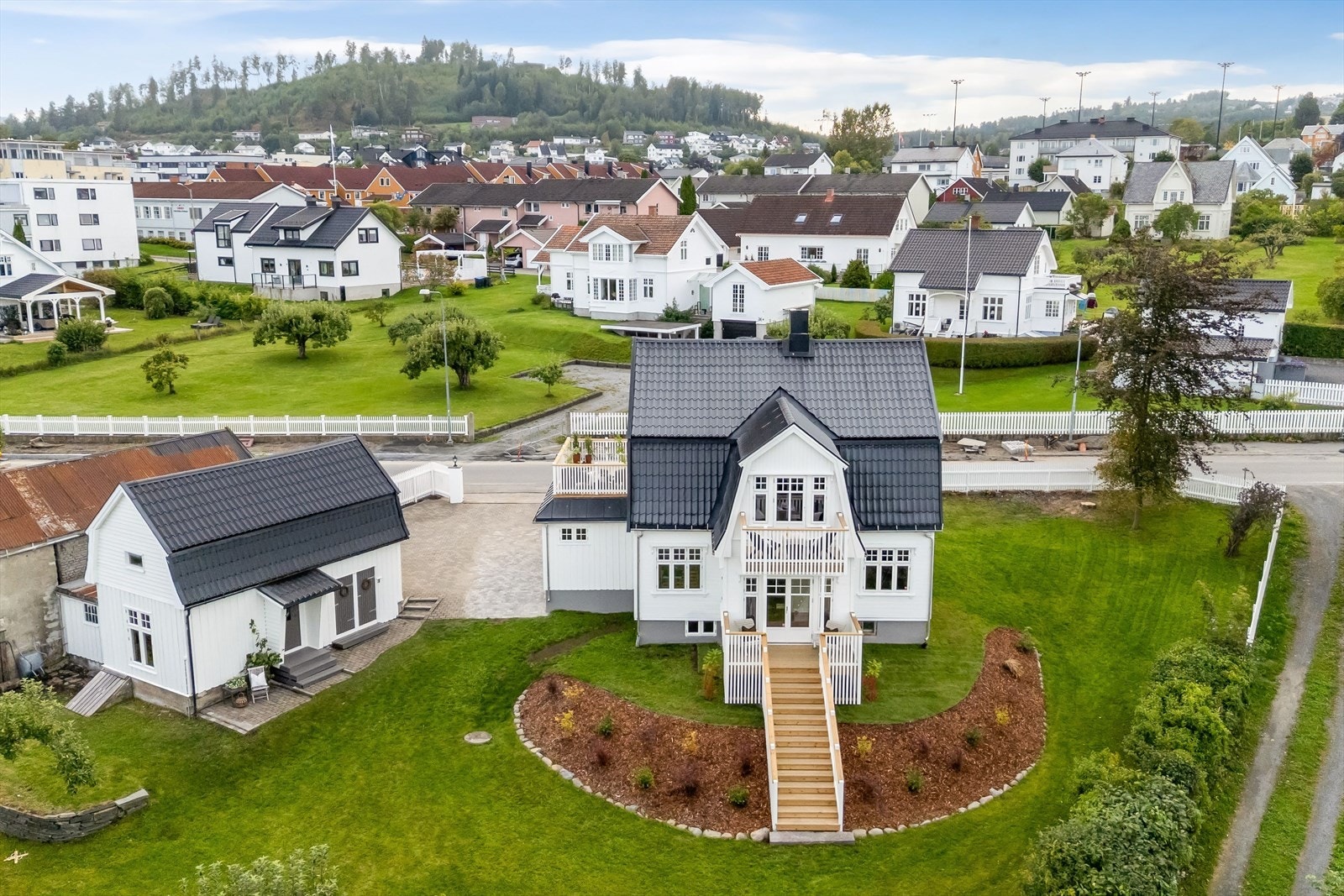 Vakker, herskapelig villa med klassisk arkitektur, hvit fasade, sort tak og en velstelt hage med prydbed og plen. Galleribilde