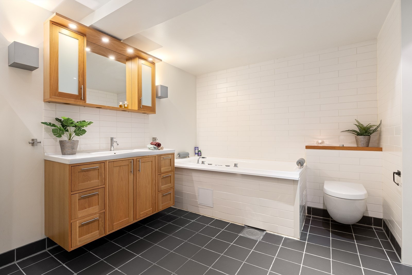 Lekkert flislagt spa-bad med boble- og massasjebadekar, dusjnisje, vegg-hengt wc samt opplegg for vaskemaskin og tørketrommel. Galleribilde