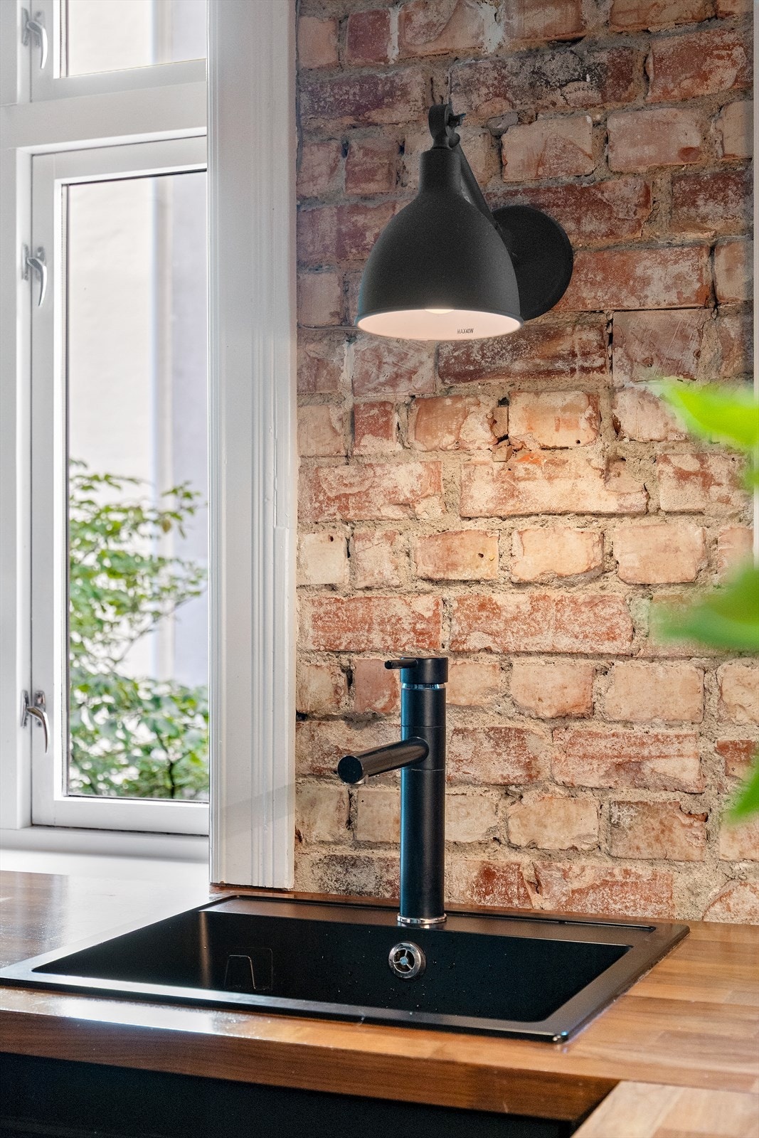 Kjøkken med moderne detaljer, inkludert svart armatur og vegglampe. Godt med naturlig lys fra vindu mot grønt uteområde. Galleribilde