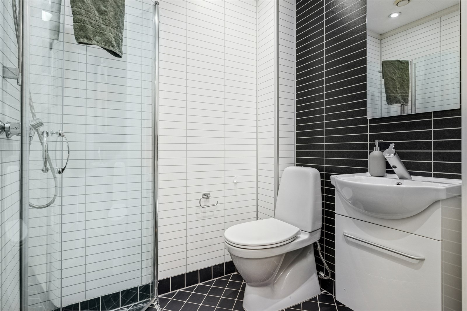 Det er 2 bad i boligen. Dette badet ligger like innenfor inngangspartiet i 1. etasje og har innfellbare dusjvegger av glass, gulvmontert toalett og servant. Galleribilde