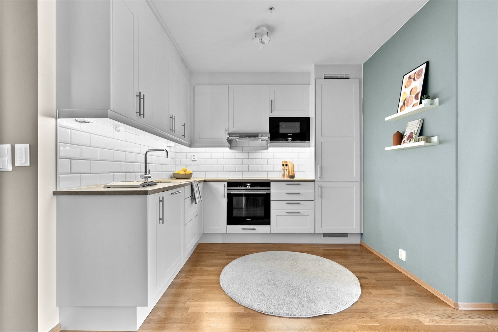Innredning med profilerte fronter og laminat benkeplate med nedfelt vask. Fliser og belysning over benkeplate. Overskap med takhøy foring gjør at det ikke samler seg fett og smuss over skapene. Galleribilde
