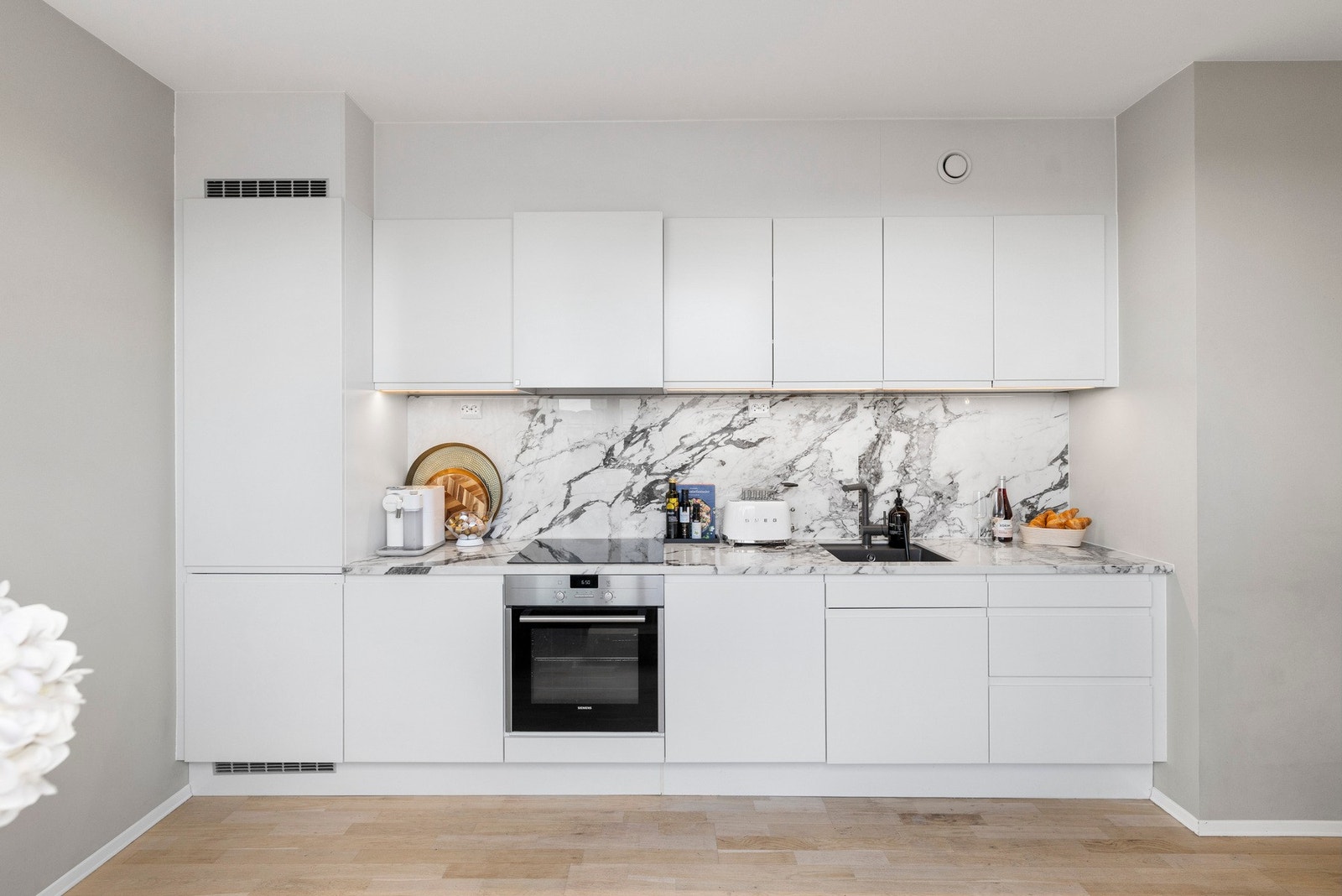 - Lekkert kjøkken med glatte fronter og marmor benkeplate med integrert kjøkkenkum. Marmor på vegg over kjøkkenbenk. Integrerte hvitevarer med innfelt platetopp i benkeplate, oppvaskmaskin, komfyr og kjøl/frys - Galleribilde