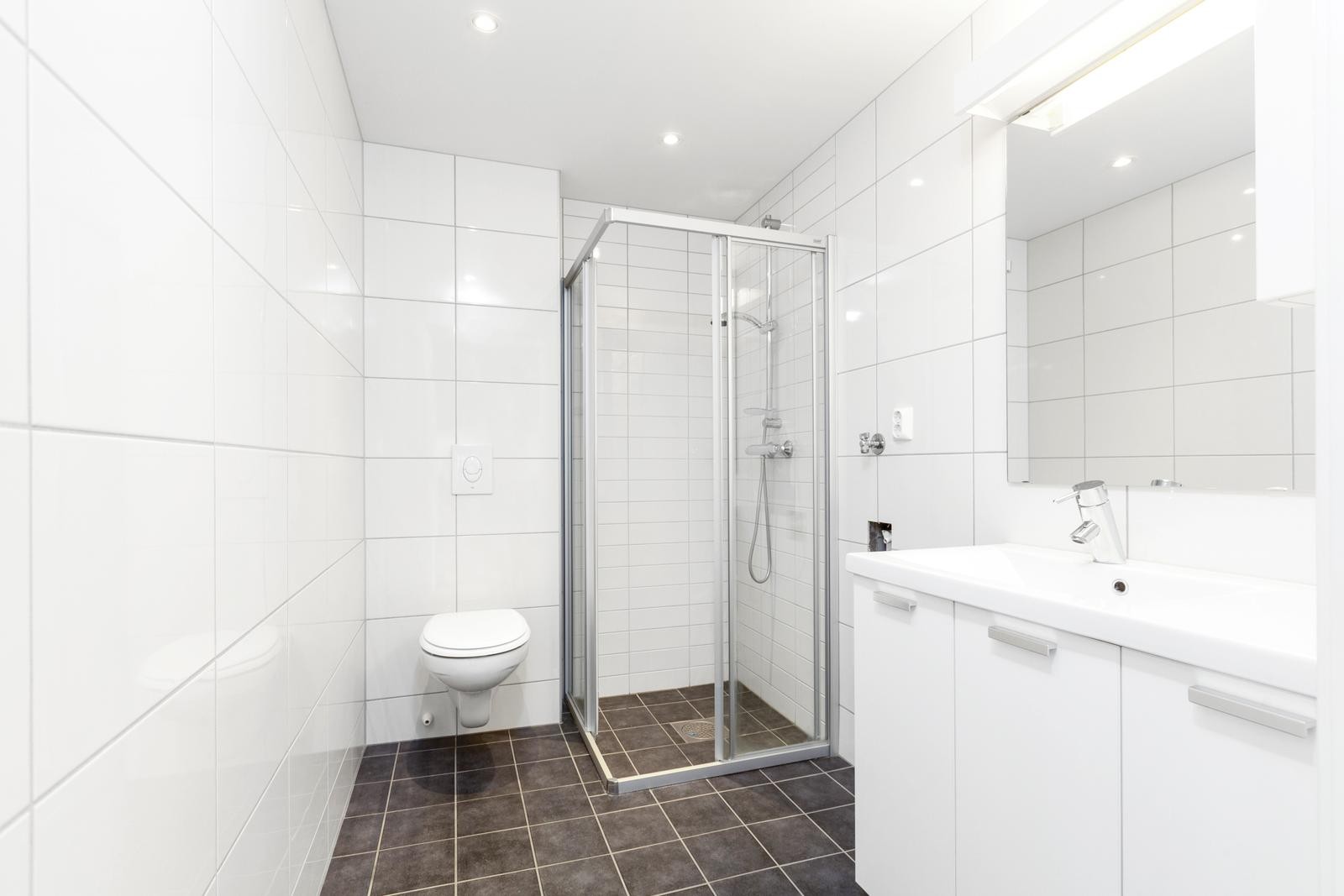 Pent flislagt bad med varme i gulv, vegghengt klosett, servant med underskap og dusjkabinett. Galleribilde