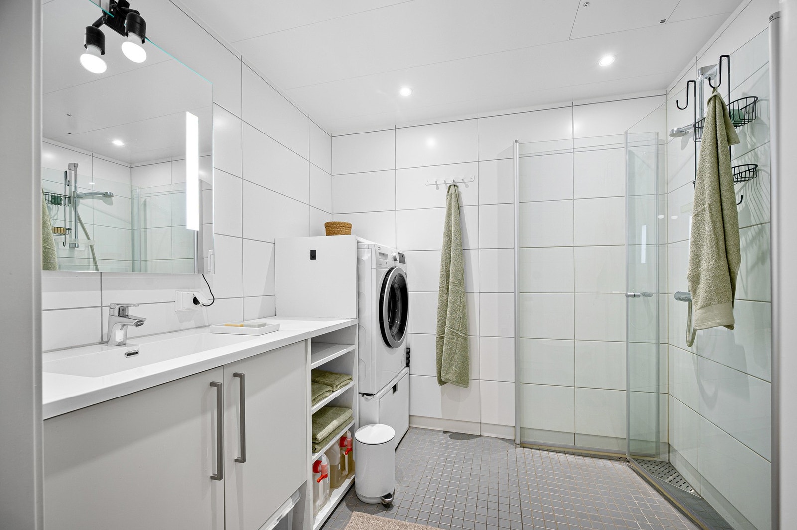 Moderne baderom med flislagte overflater, dusjhjørne i glass, vegghengt innredning, WC og opplegg for vaskemaskin. Galleribilde