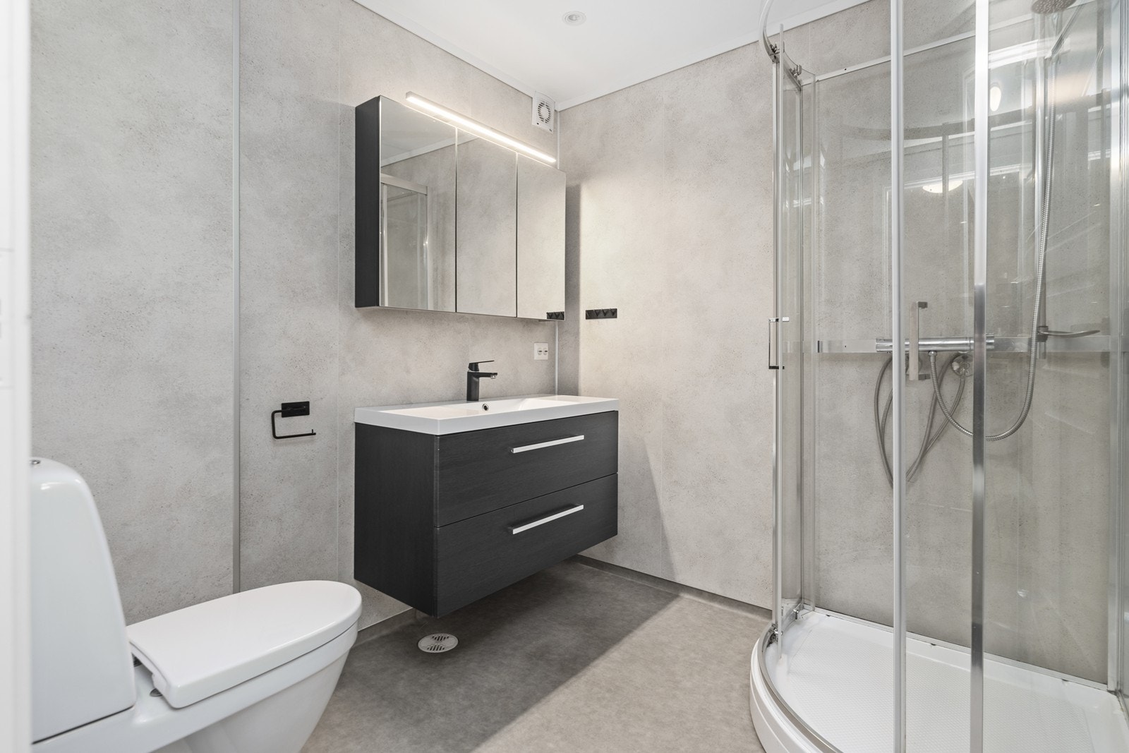 Bad har belegg på gulv og baderomsplater på vegger. Rommet inneholder dusjkabinett, innredning med nedfelt servant og toalett. Galleribilde