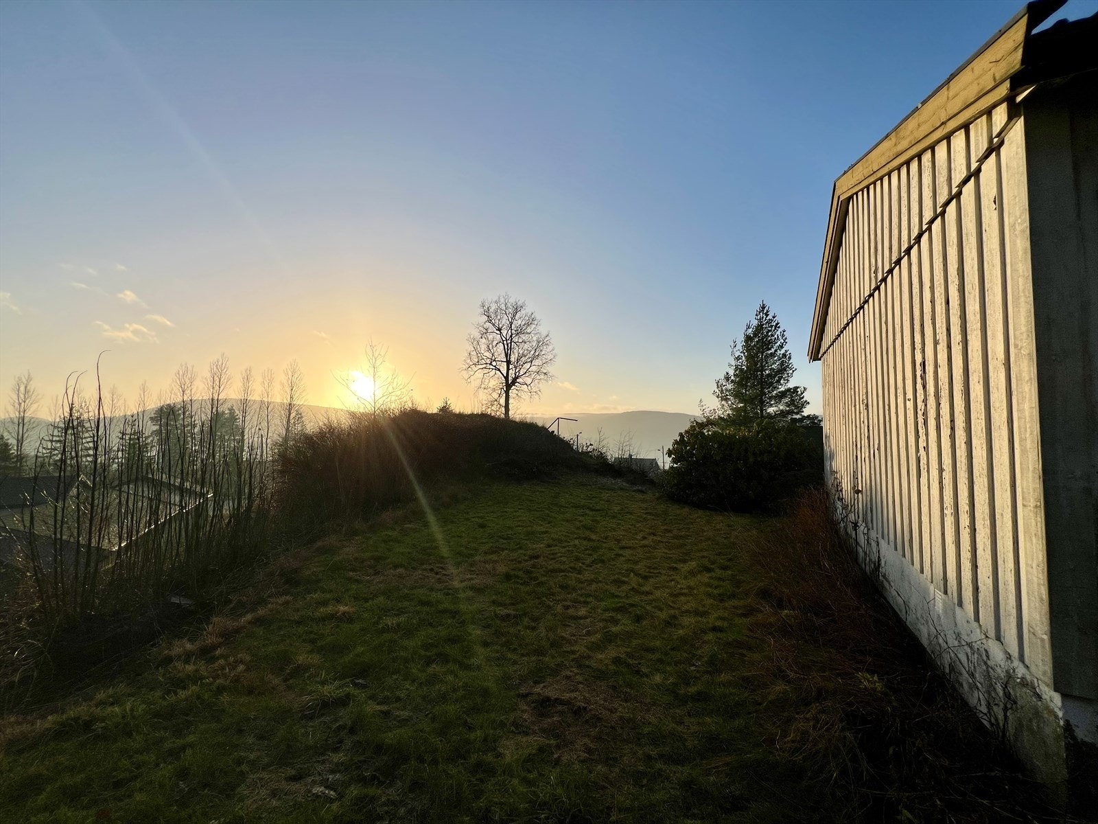 Boligen ligger fint til på en skrående tomt som er opparbeidet med plen, trær og prydbusker. Galleribilde