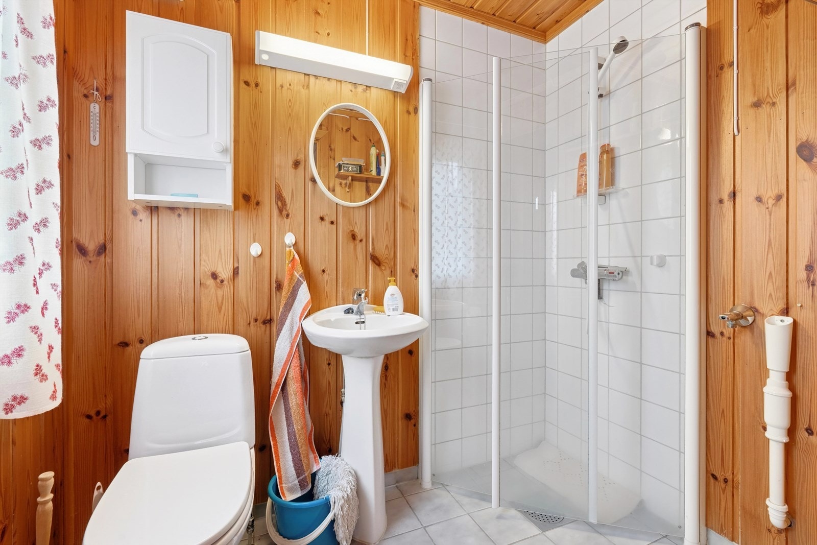 Badet i 1. etasje er fra 2000, og har flislagt gulv, furupanel på vegger og fliser i dusjhjørnet. Det er opplegg for vaskemaskin og tørketrommel, og rommet har elektrisk styrt avtrekksvifte montert i vegg. Galleribilde