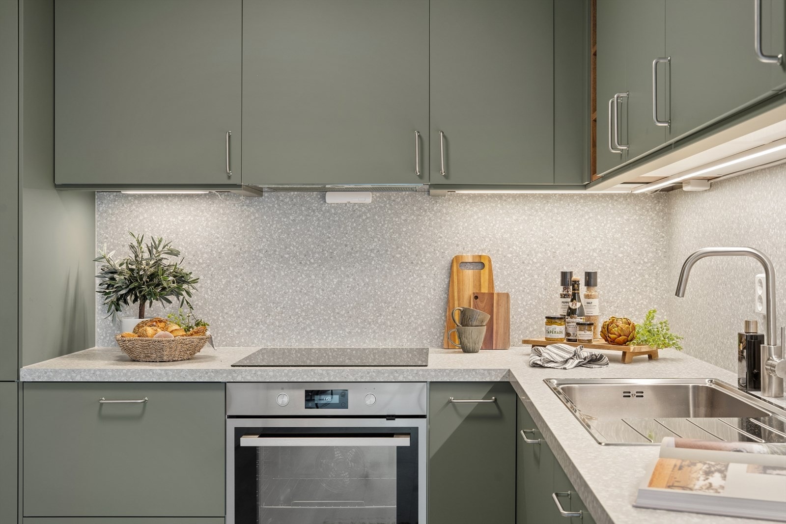 Det er en vaskekum i stål med avrenning, ettgreps blandebatteri og belysning under overskapene. Veggen over kjøkkenbenken er kledd med laminatplater. Galleribilde