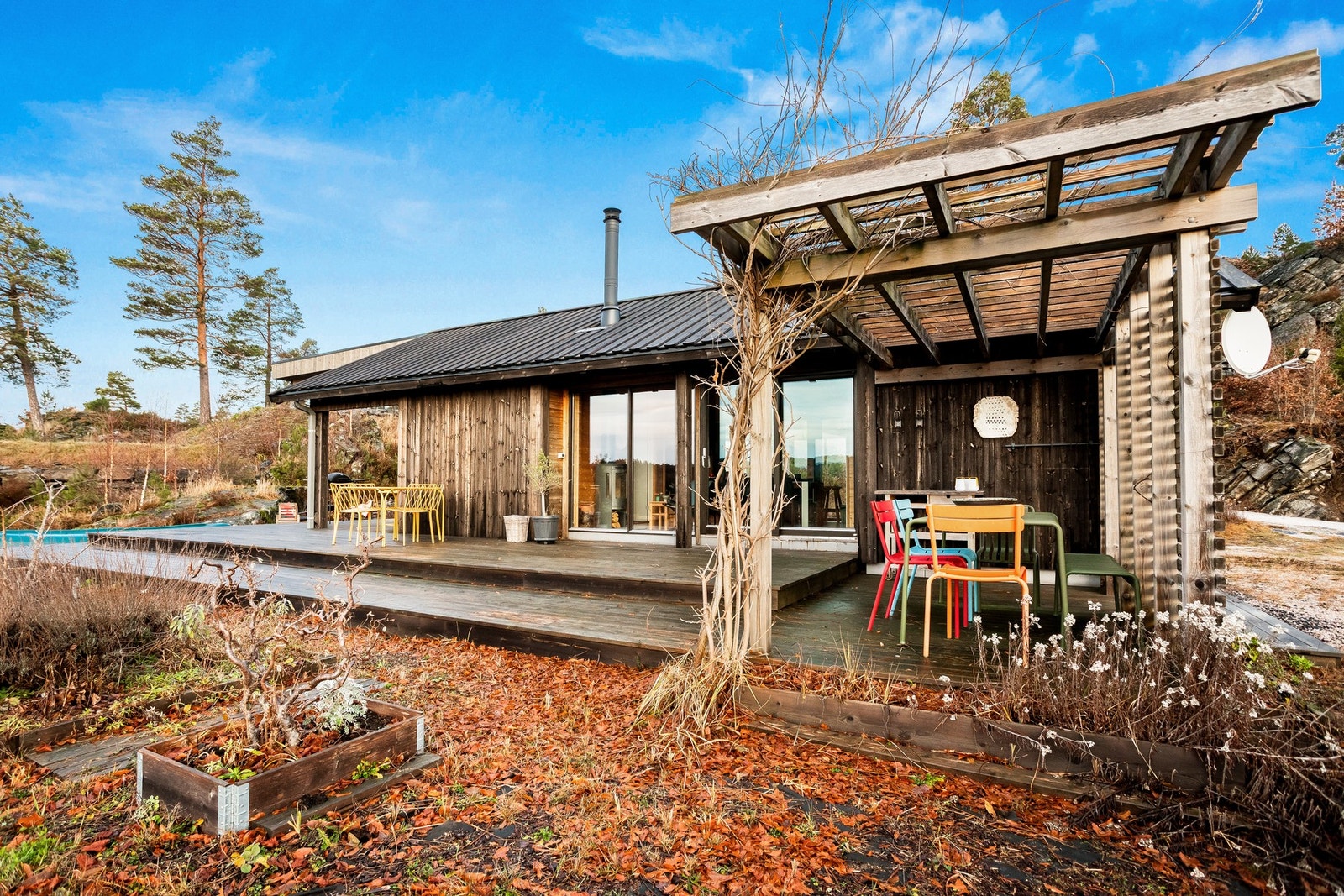 Romslig terrasse som strekker seg rundt store deler av hytta mot vannet. Galleribilde