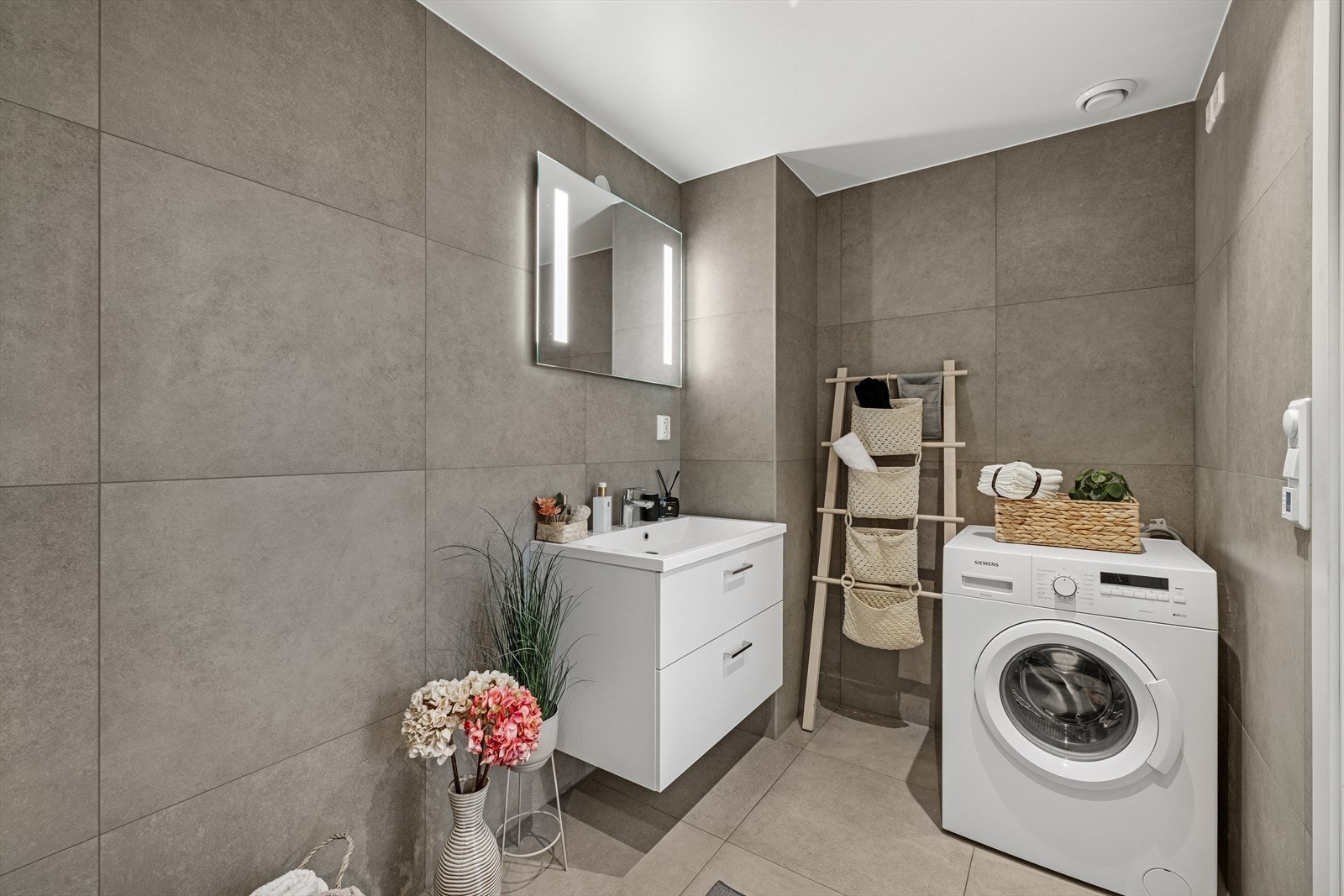 Baderom består av dushjørne, opplegg for vaskemaskin, underskap, toalett og speil med integrert belysing. Galleribilde