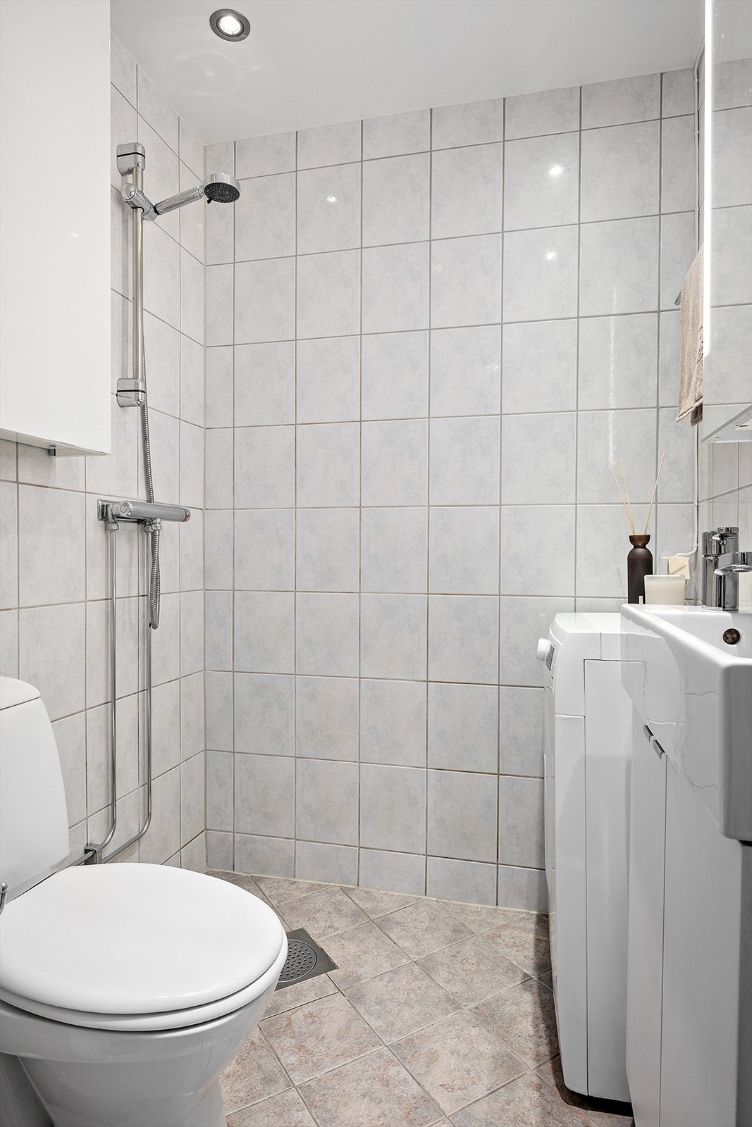 Badet har flislagte overflater, veggskap ved dusj samt baderomsinnredning bestående av benkeskap og veggskap med speil og belysning over servant. Det er dusj på gulv, gulvstående klosett og servant, samt opplegg for vaskemaskin. Galleribilde