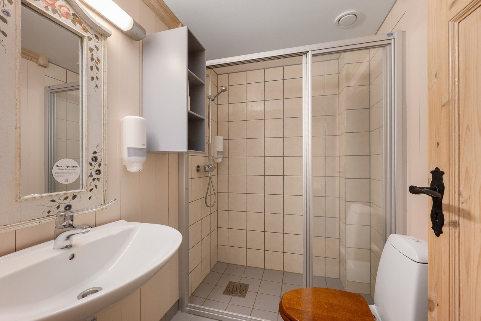 Baderommet har fliser på gulv, fliser og panel på vegger. Servant. Speil med tilhørende belysning. Dusjvegger. Gulvmontert wc. Mekanisk avtrekk. Galleribilde