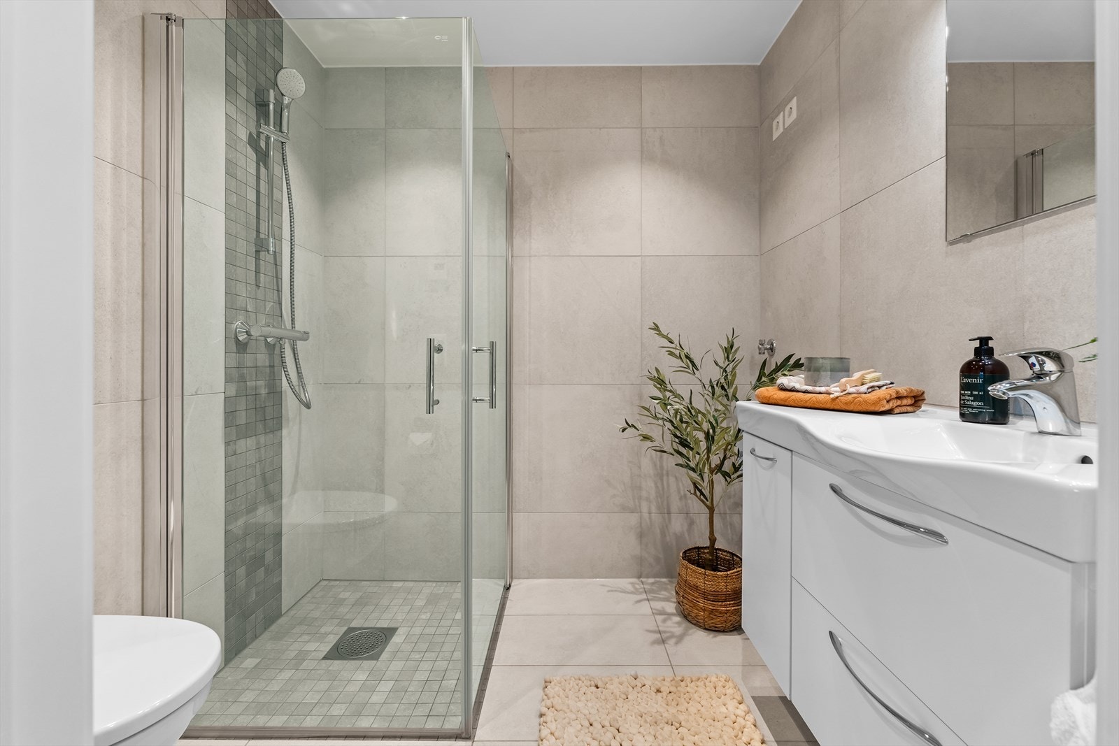 Delikat flislagt bad i 1. etasje med gulvvarme. Badet er innredet med servant i baderomsinnredning, toalett og dusjhjørne med innfellbare glassvegger. Det er opplegg for vaskemaskin. Galleribilde