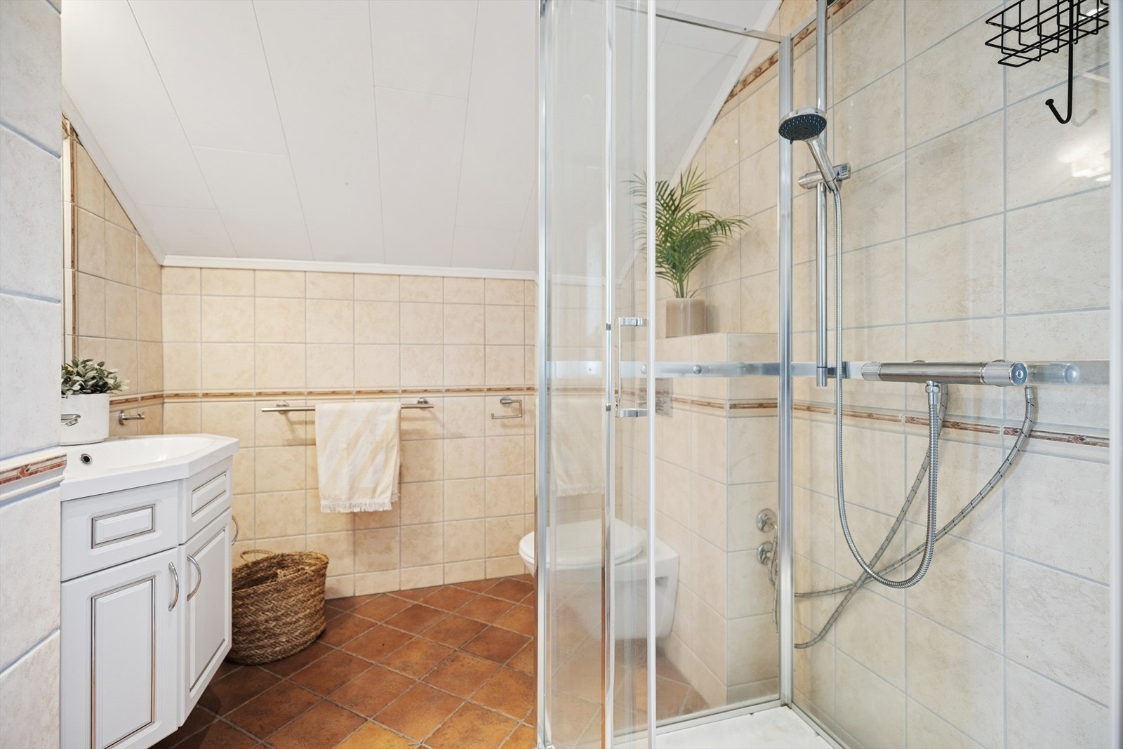 Rommet er utstyrt med et vegghengt toalett, servant med servantskap, speil og et dusjkabinett. Galleribilde