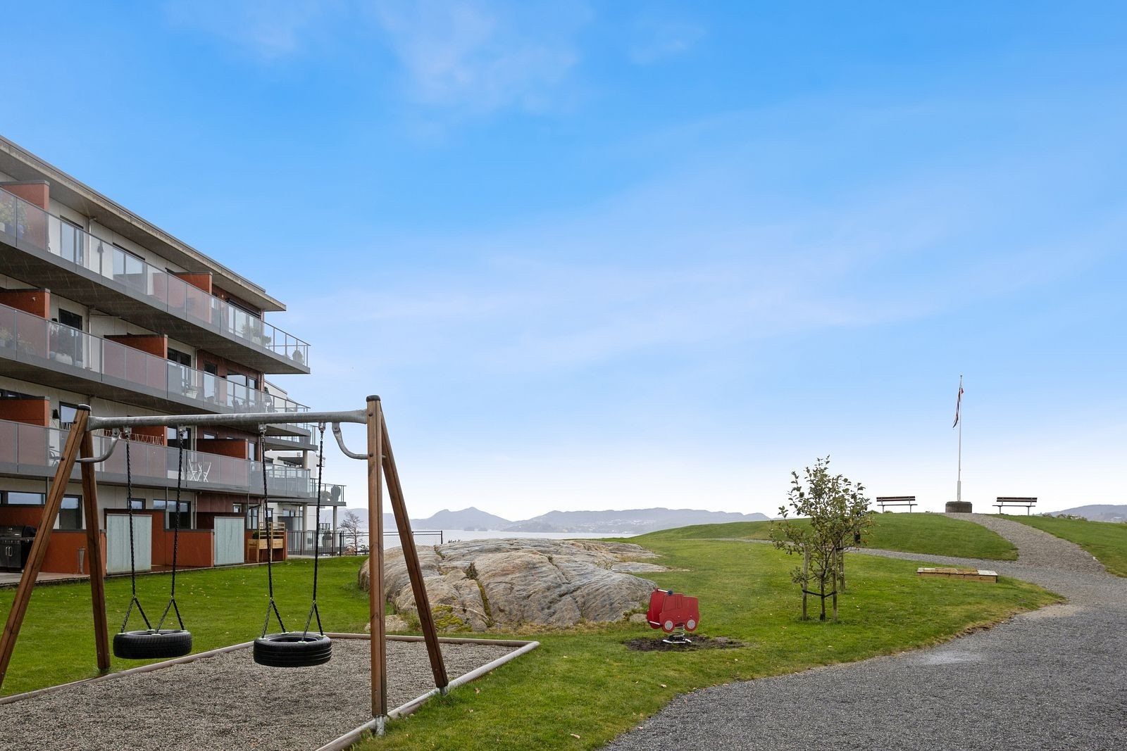 Fellesområde med lekeplass og sitteplasser, beplantning og gruset internveier. Galleribilde