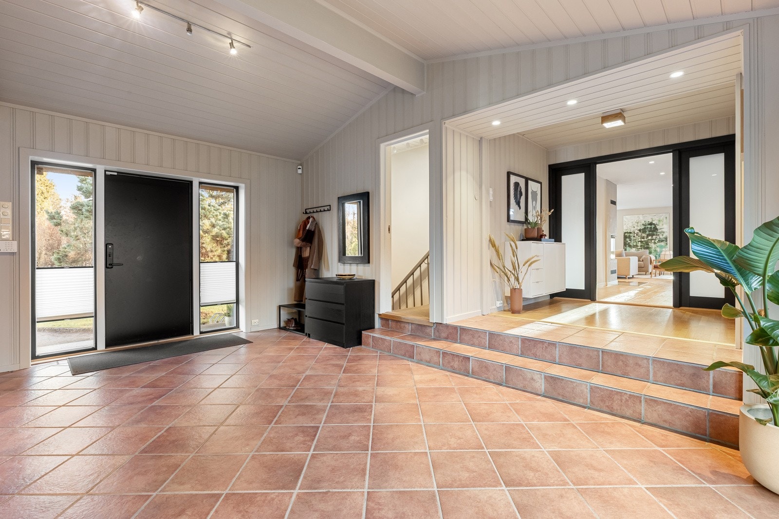 1. etasje: Fra den luftige entrèen går du videre inn i stuen eller trappen ned til boligens u. etasjen. Store vindusflater på begge sider av inngangsdøren Galleribilde