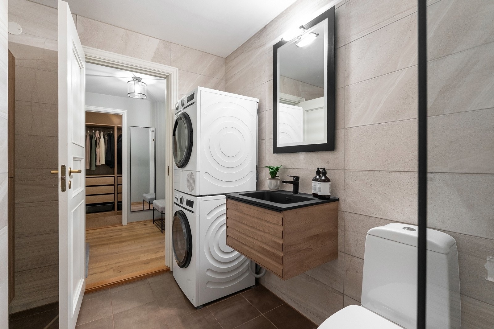 Rommet har servant med profilerte fronter, gulvstående toalett, dusjhjørne og opplegg for vaskemaskin og tørketrommel Galleribilde