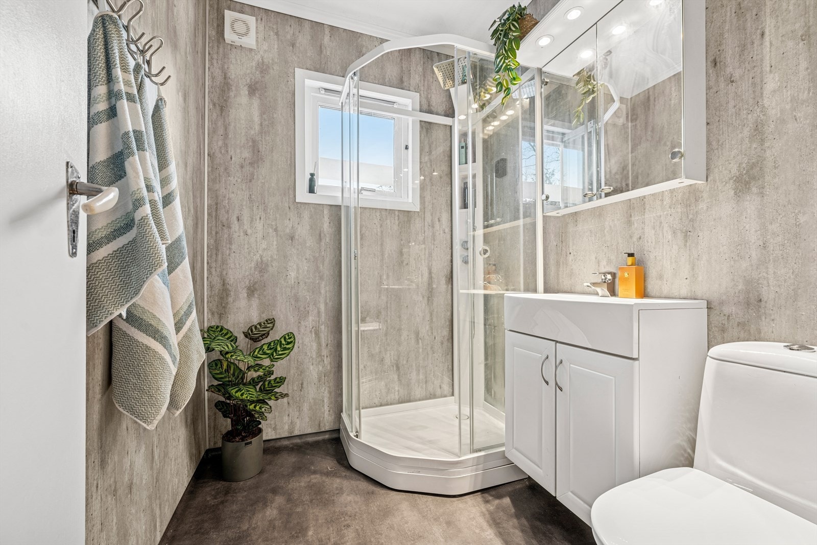 Bad med baderomsplater på vegger og belegg på gulv. Badet har baderomsinnredning med heldekkende servant og speil på vegg, gulvmontert wc og dusjkabinett. Galleribilde